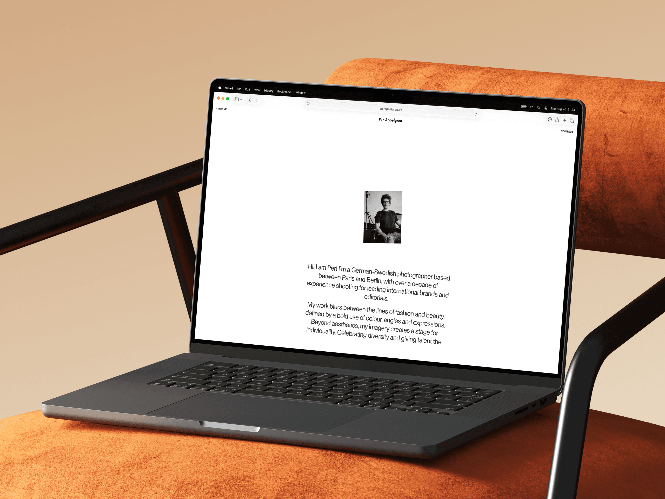 Laptop on an orange armchair showing the website intro: a black-and-white portrait of the photographer above his bio.