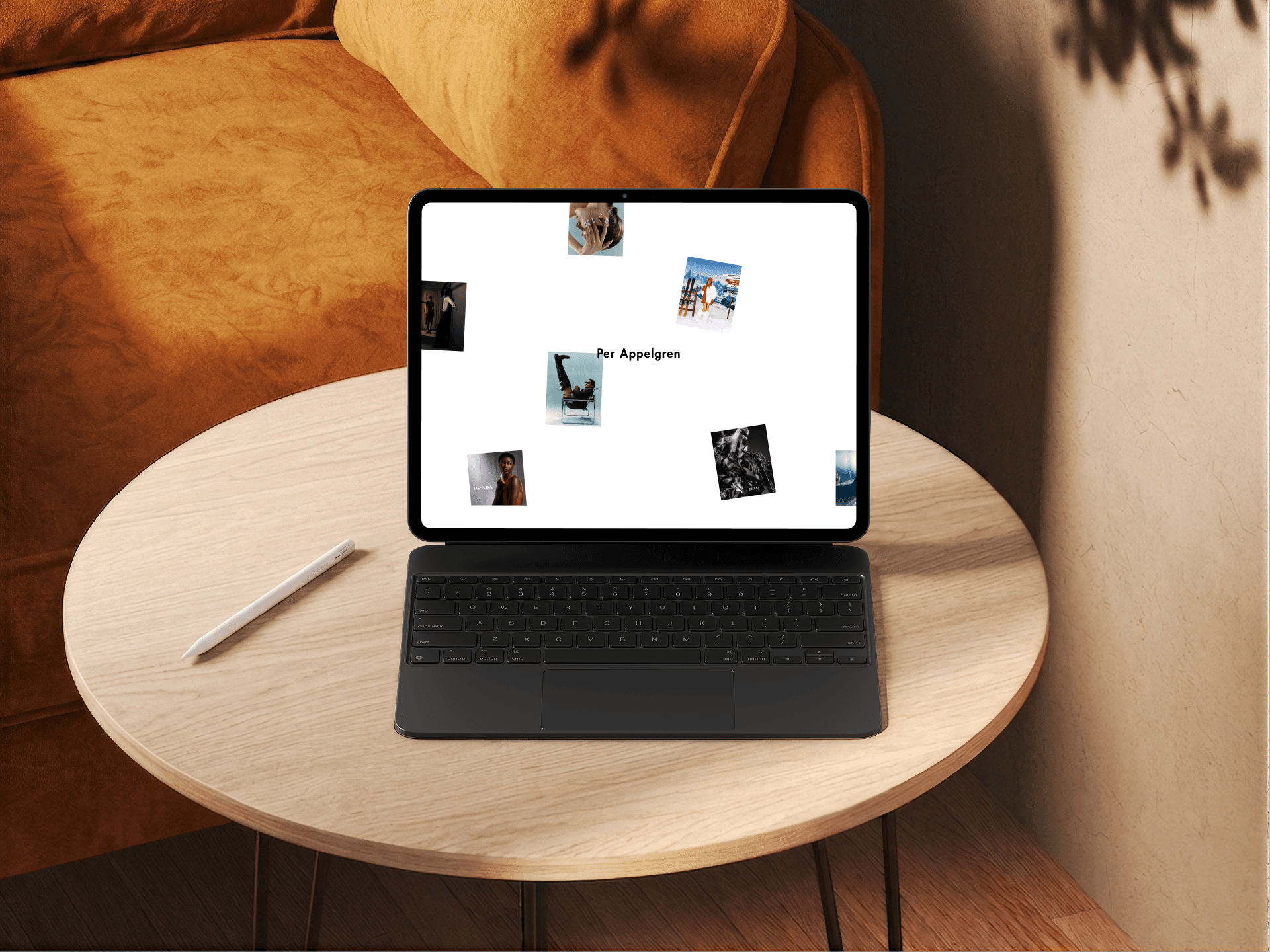 Tablet on a round wooden table showing the Per Appelgren preloader, with the name in the center and campaign photos scattered around it.