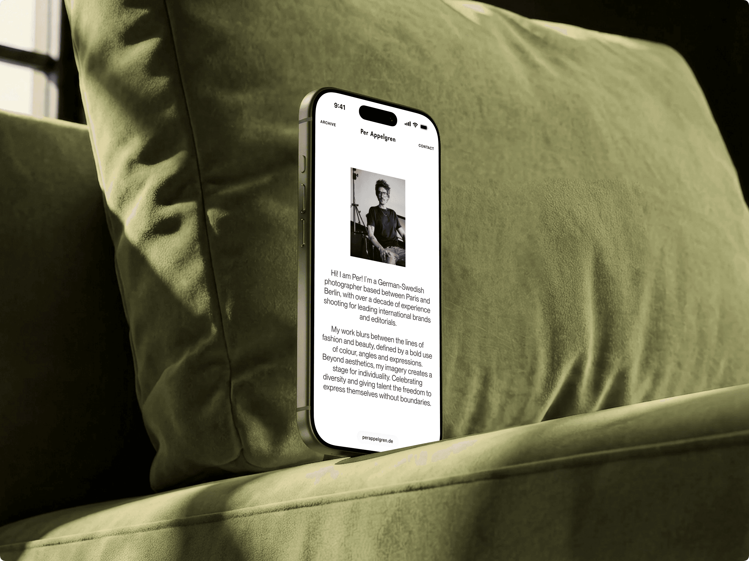Smartphone on a green sofa showing the mobile intro: a black-and-white portrait of the photographer above his bio.